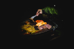 Hands working over a hot barbecue grill with heat-resistant gloves