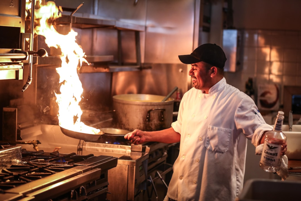 Chef using high heat to sear food in a kitchen